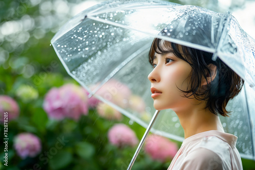 雨が降る中、傘を差して空を見上げている若い日本人女性（紫陽花の背景）