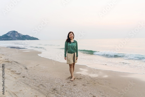 A woman walks along the sunny beach, enjoying the ocean waves