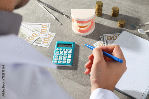 Man with pen in hand, notepad, cash, calculator, jaw and dental instruments on gray background
