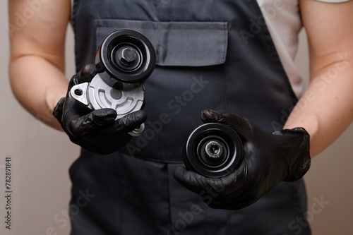 An auto mechanic holds in his hands in black gloves a idler pulley with a tensioner for a car's poly V-belt and a parasitic roller, close-up. Auto parts replacement concept, car maintenance. photo