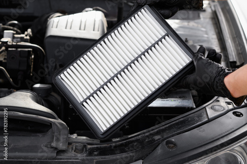 Auto mechanic holds car air filter in his hands near engine compartment, close-up. Concept of replacing auto parts, replacing air filter, car maintenance, protection from allergens, dirt,soot,viruses.