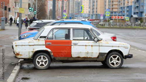 An old white rusty Soviet car with a red door is parked on the street, Soyuzny Prospekt, St. Petersburg, Russia, April 12, 2024