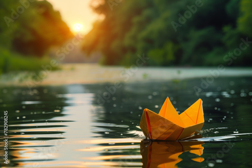 Yellow paper boat on reflective water at sunset, casting a warm glow with a backdrop of dense foliage photo