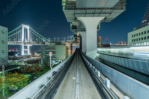Night POV shot from Yurikamome train with architectural landmark Rainbow Bridge in the distance in Tokyo, Japan.