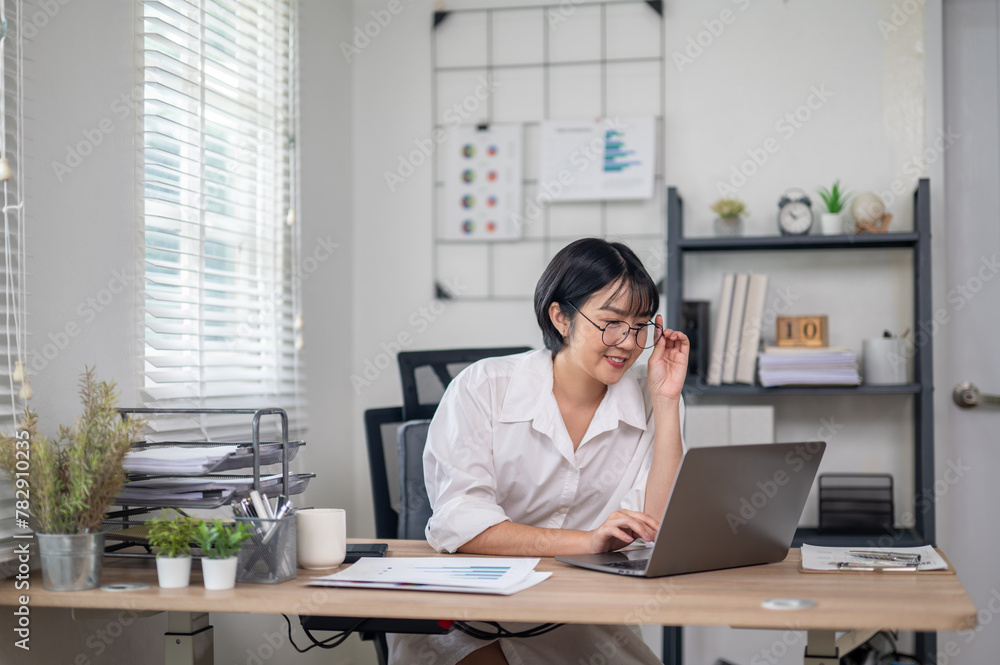 Cheerful businesswoman in white shirt using smartphone with laptop and documents on her office desk. Cheerful businesswoman in white shirt using smartphone with laptop and documents on her office desk.
