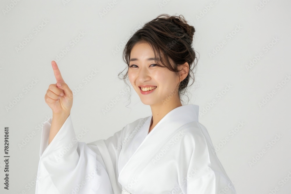 A beautiful Asian woman is smiling, showing with finger, wearing white against a white background in the style of professional photography with sharp focus. A beautiful Asian woman is smiling, showing with finger, wearing white against a white background in the style of professional photography with sharp focus.