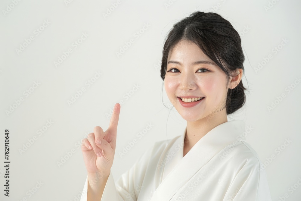 A beautiful Asian woman is smiling, showing with finger, wearing white against a white background in the style of professional photography with sharp focus. A beautiful Asian woman is smiling, showing with finger, wearing white against a white background in the style of professional photography with sharp focus.