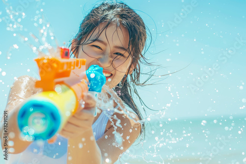 Happy traveler asian woman wearing summer shirt holding colorful squirt water gun over blur sea, Water festival holiday concept