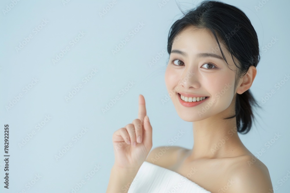 Portrait of a beautiful smiling Asian woman in a white dress, pointing her finger up to the side on an empty light background. Portrait of a beautiful smiling Asian woman in a white dress, pointing her finger up to the side on an empty light background.