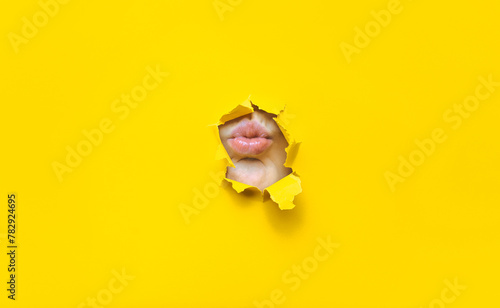 A child's lips appear in a torn hole of yellow paper. Imitation of a kiss. Silence concept. photo