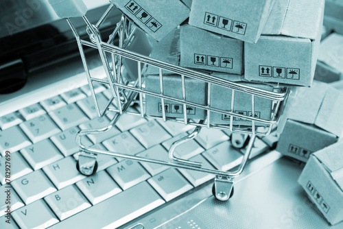 Shopping trolley and shipping carton boxes on laptop computer keyboard. Online shopping and selling concept. 