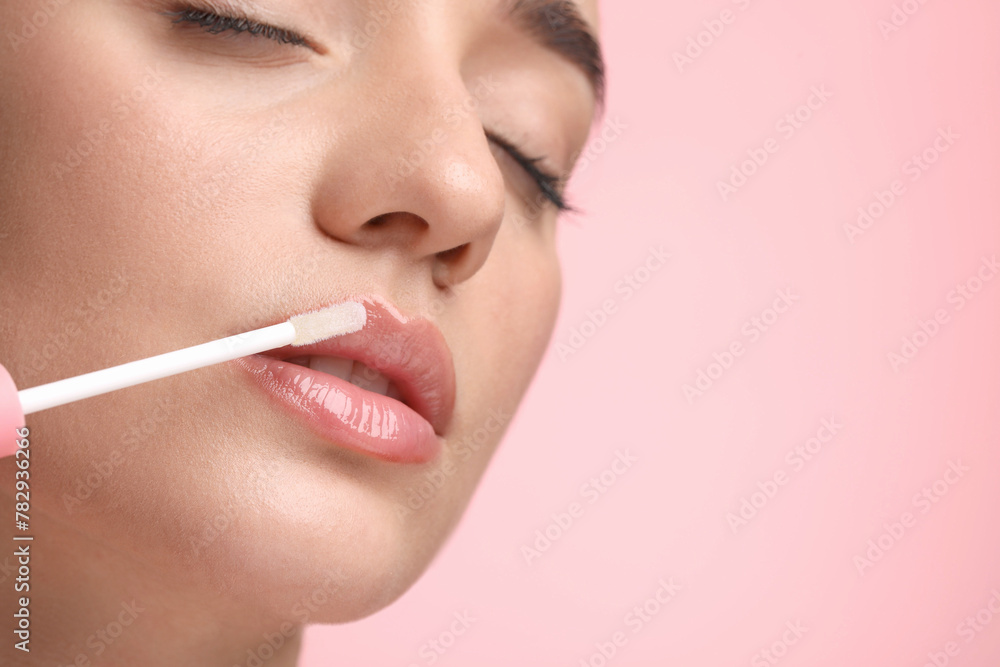 Woman applying lip gloss on pink background, closeup. Space for text Woman applying lip gloss on pink background, closeup. Space for text