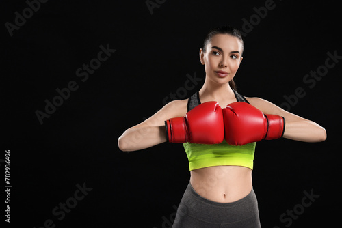 Portrait of beautiful woman in boxing gloves on black background. Space for text
