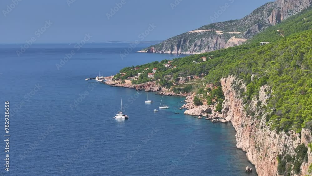 AERIAL: Scenic drone view of sailboats near the lush green Hvar island at the peak of summer. Sailboats are anchored In a breathtaking secluded bay next to the coast of island in the Mediterranean. AERIAL: Scenic drone view of sailboats near the lush green Hvar island at the peak of summer. Sailboats are anchored In a breathtaking secluded bay next to the coast of island in the Mediterranean.