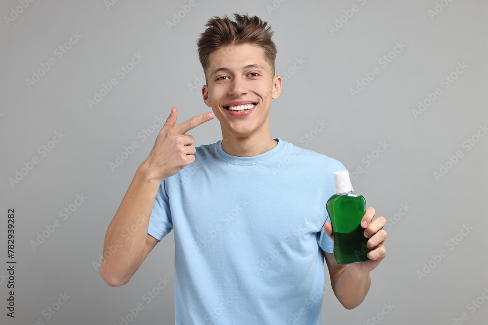 Young man with mouthwash pointing at his healthy teeth on light grey background Young man with mouthwash pointing at his healthy teeth on light grey background