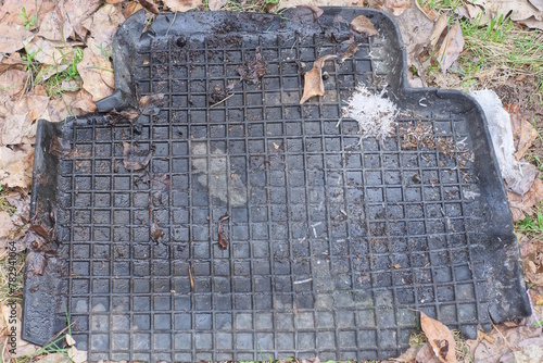one dirty rubber black car mat lies on the gray ground on the street
