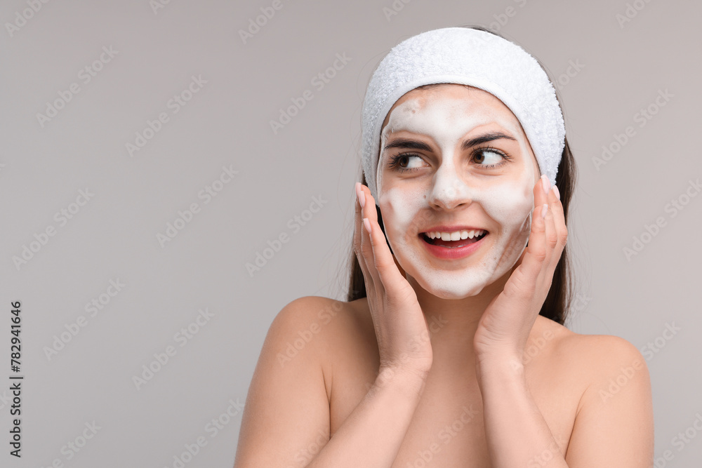 Young woman with headband washing her face on light grey background, space for text Young woman with headband washing her face on light grey background, space for text