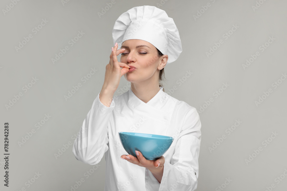 Woman chef in uniform holding bowl and showing perfect sign on grey background Woman chef in uniform holding bowl and showing perfect sign on grey background