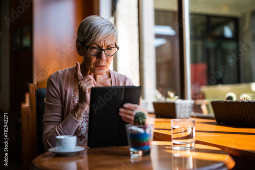 Mature woman is sitting in cafe and using digital tablet.