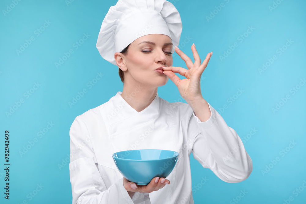 Woman chef in uniform holding bowl and showing perfect sign on light blue background Woman chef in uniform holding bowl and showing perfect sign on light blue background