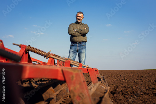 Portrait of satisfied mature farmer standing in field preparing to cultivate the land with a tractor.