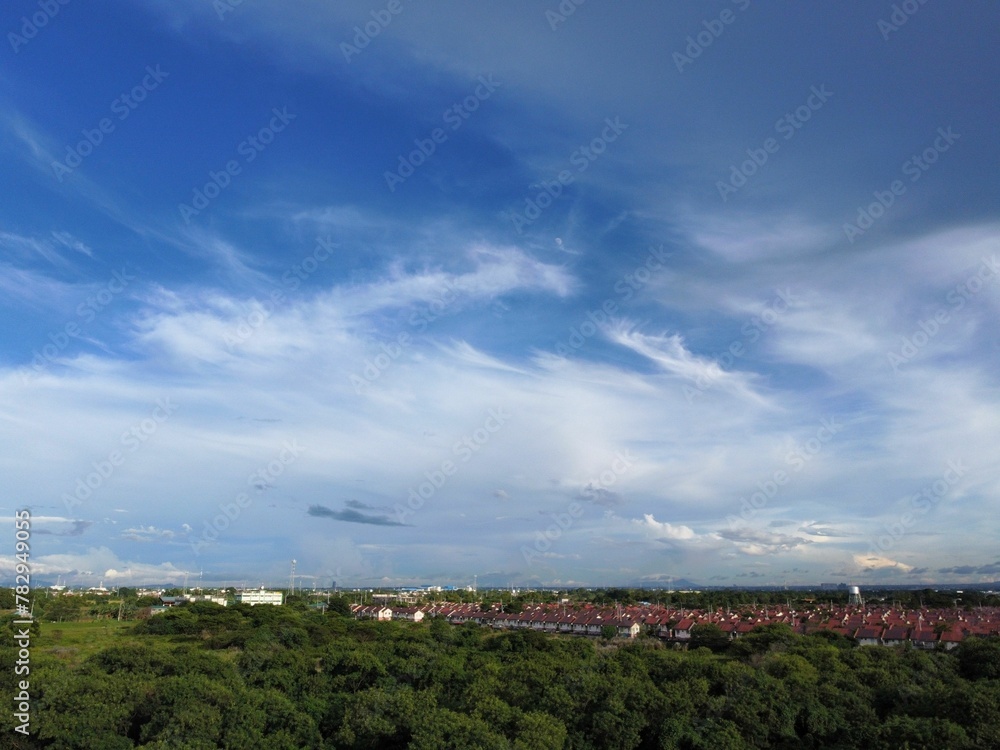 Aerial view of lush green field in a rural area under blue cloudy sky with buildings in background