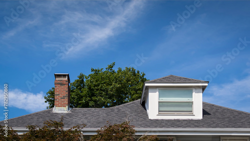 Hip dormer and brick chimney on the sloped shingle roof of a family house in Boston, MA, USA