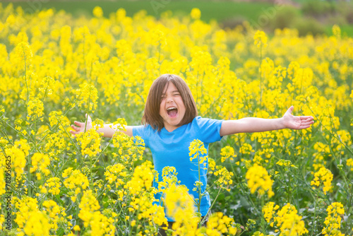 Five-year-old boy screaming with open arms in a rapeseed meadow.