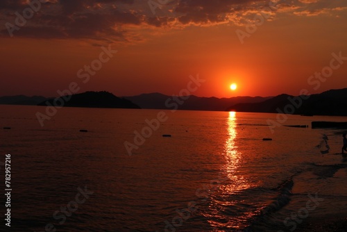 the sun rises over the ocean and waves and a beach chair