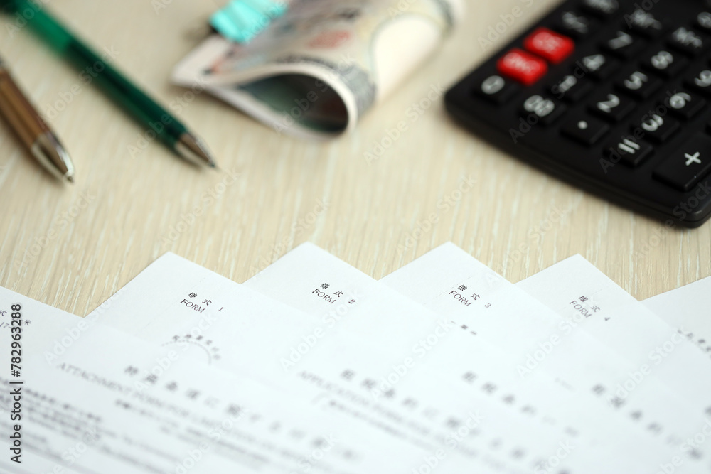 Japanese tax forms lies on table with calculator, pen and japanese yen money bills roll close up Japanese tax forms lies on table with calculator, pen and japanese yen money bills roll close up