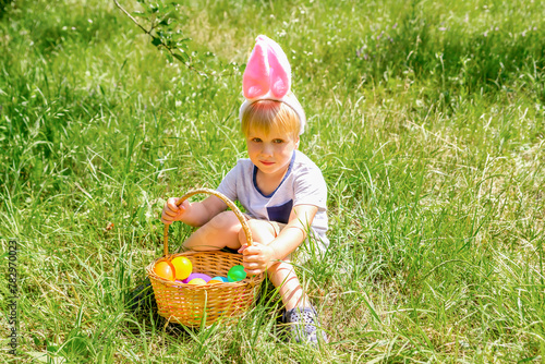 Easter egg hunt. Little boy child kid in bunny ears having fun,picking up eggs in grass,in garden. Easter holiday tradition. Baby with basket full of colorful eggs © Дарья Воронцова