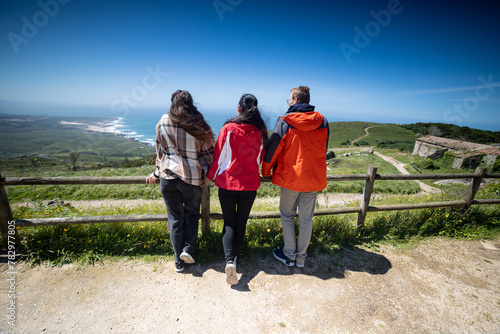 Three People Standing on Hill Overlooking Ocean