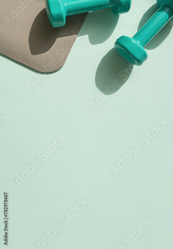 Sport or workout concept flat lay with blue dumbbells and yoga mat on the blue background. Copy space