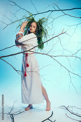 A young woman in a white dress and traditional outfit stands gracefully in front of a mystical tree in a studio setting. © LIGHTFIELD STUDIOS