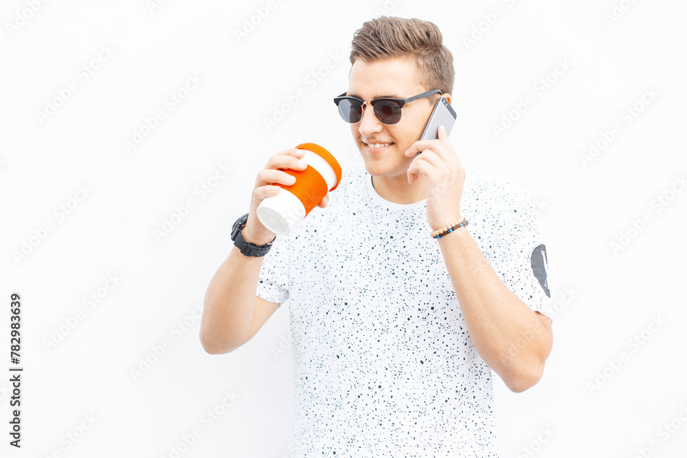 Happy successful handsome guy talking on the phone and drinking coffee on a white background on the street Happy successful handsome guy talking on the phone and drinking coffee on a white background on the street