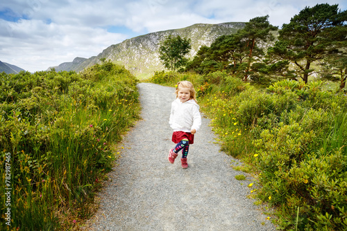 Cute little happy toddler girl running on nature path in Glenveagh national park in Ireland. Smiling and laughing baby child having fun spending family vacations in nature. Traveling with small kids