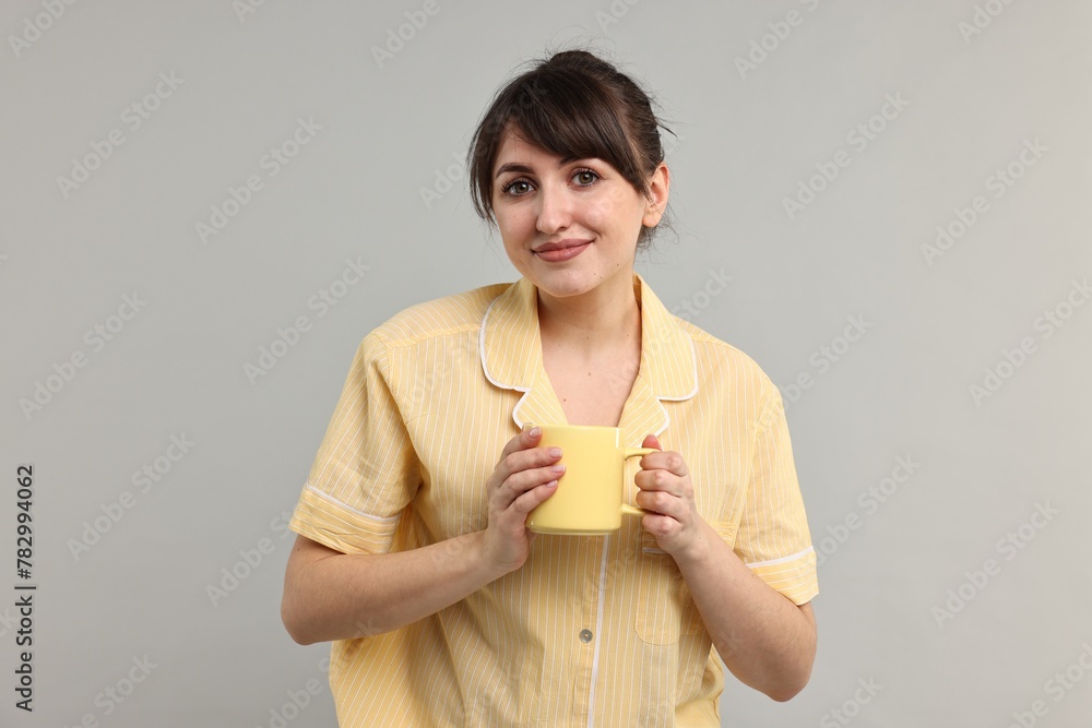 Woman in pyjama holding cup of drink on grey background Woman in pyjama holding cup of drink on grey background