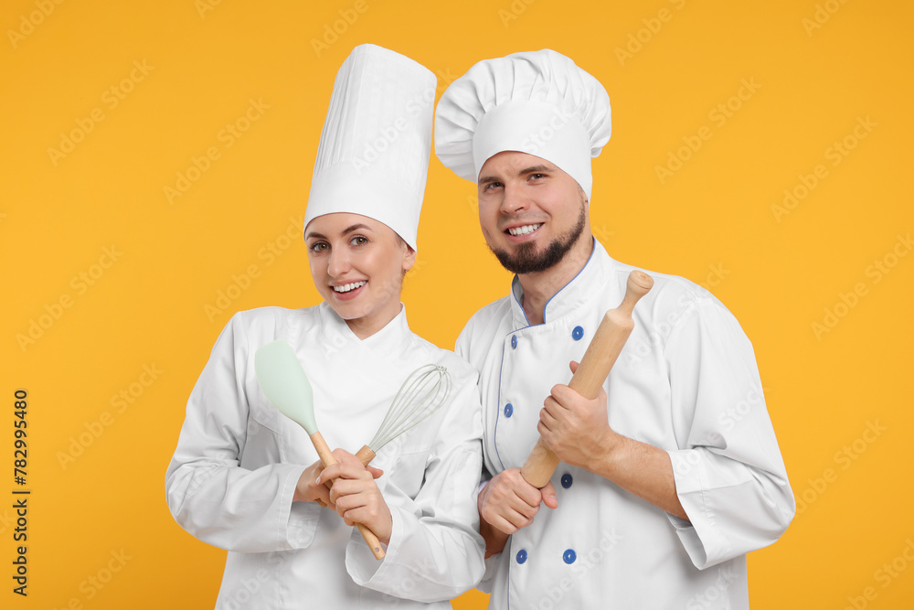 Happy confectioners in uniforms holding professional tools on yellow background Happy confectioners in uniforms holding professional tools on yellow background