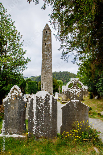 Stone round tower and some ruins of a monastic settlement originally built in the 6th century in Glendalough valley, County Wicklow, Ireland on sunny day