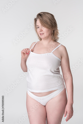 Confident Caucasian model from generation X wearing white cotton camisole and panties. Her serious expression exudes authority and control, showcasing her expertise as an overweight fashion model