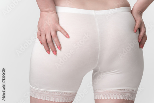 Unidentified middle aged woman is shown in closeup rear view wearing pantaloons and placing her palms on buttocks. Image represents concepts of body consciousness and body positivity in adulthood