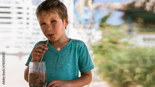 Happy childhood. Boy drinking chocolate tea with ice in hot summer day time. Cute lover of sweets and tasty things