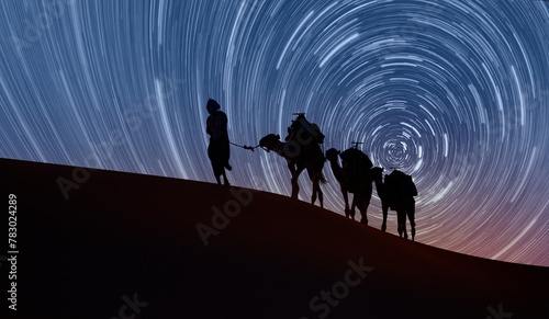 Camel caravan in the desert - Long exposure photo of night sky star trail over the sand dunes of Sahara Desert - Sahara, Morocco