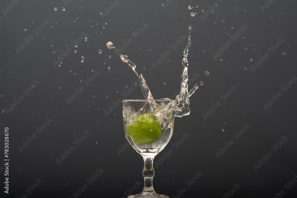 Lemon falling into a glass of transparent water causing splashes upwards. Isolated on gray background. Lemon falling into a glass of transparent water causing splashes upwards. Isolated on gray background.