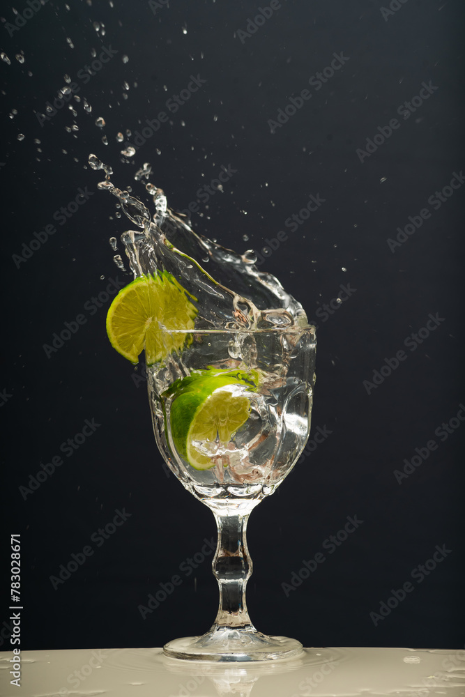 Lemon falling into a glass of transparent water causing splashes upwards. Isolated on gray background. Lemon falling into a glass of transparent water causing splashes upwards. Isolated on gray background.
