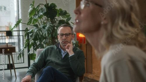 middle age male psychologist has family therapy meeting with adult couple, sitting in office with notebook and listening attentively and commenting. couple argues, has tension dispute.