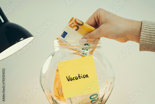 Euro banknote in hand of a person, putting it into the glass jar, toned close up photo. Vacation concept, saving money for free time and pleasure © Vitalii