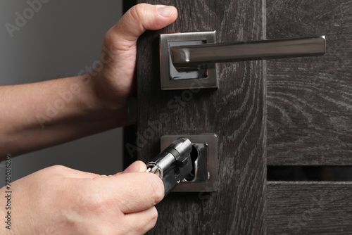 Handyman changing core of door lock indoors, closeup photo