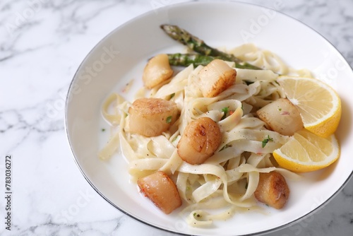 Delicious scallop pasta with asparagus and lemon on white marble table, closeup
