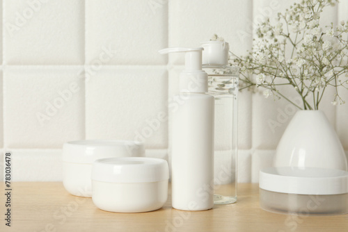 Bath accessories. Different personal care products and gypsophila flowers in vase on wooden table near white tiled wall